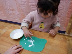 指を使って白い絵の具を緑の画用紙に塗っています