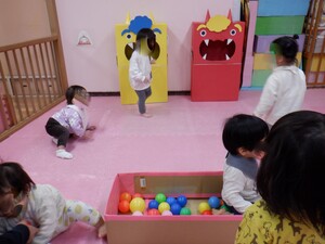 0歳児5名が、カラーボールの入った箱や鬼の顔が描いてある段ボールの近くにいます