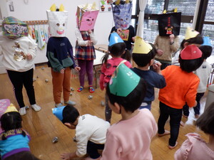 2歳児8名が横並びに立つ5歳児5名に新聞紙で作った豆を投げています